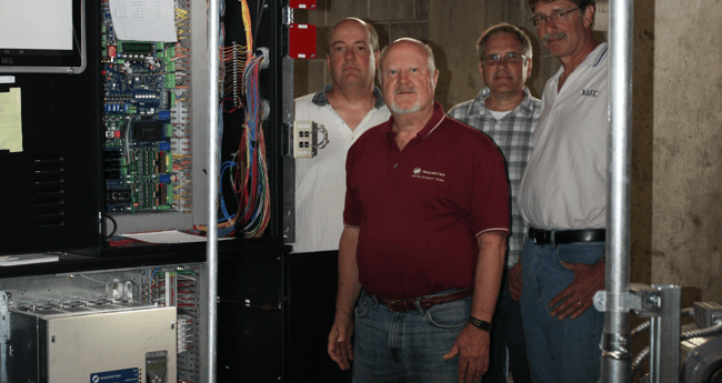 Image of four men standing behind an AC elevator drive