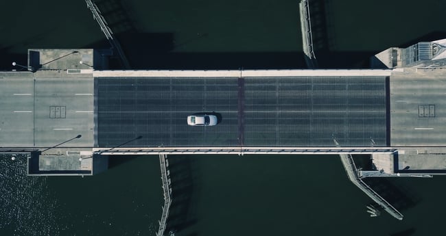 Overhead image of one white car driving across bridge 